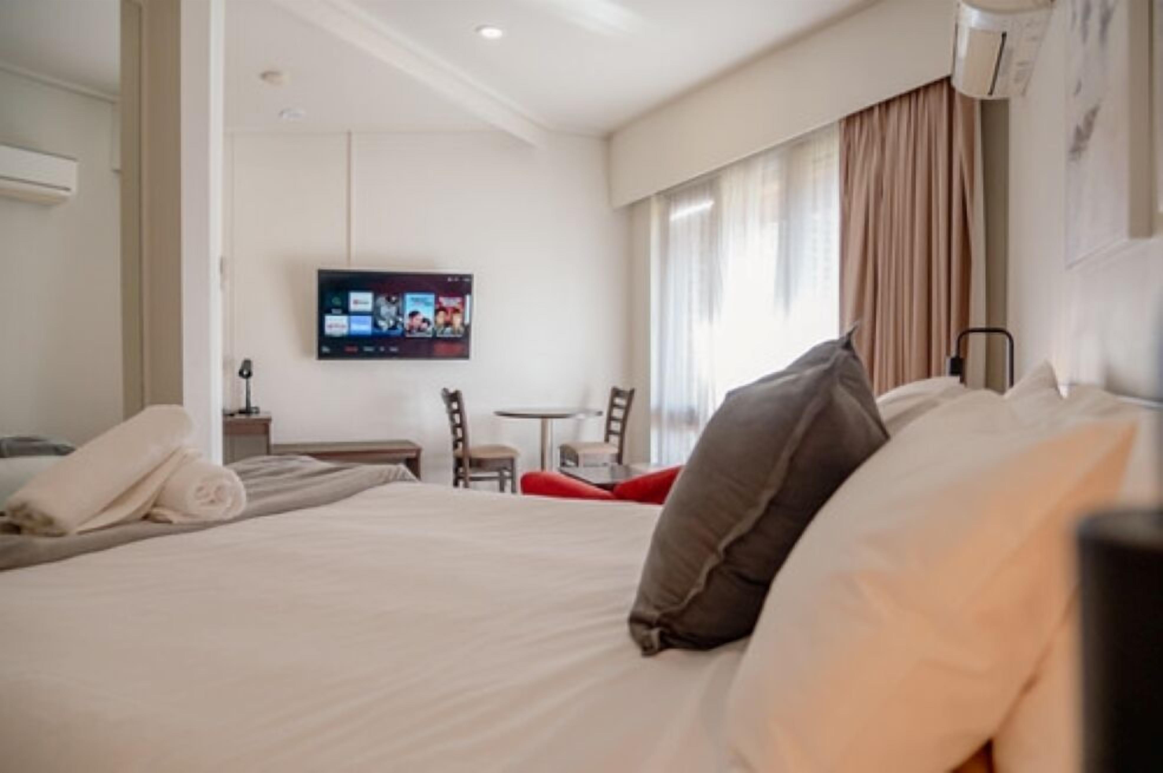 Una camera d'albergo con un letto, una TV a muro, un tavolino e sedie.