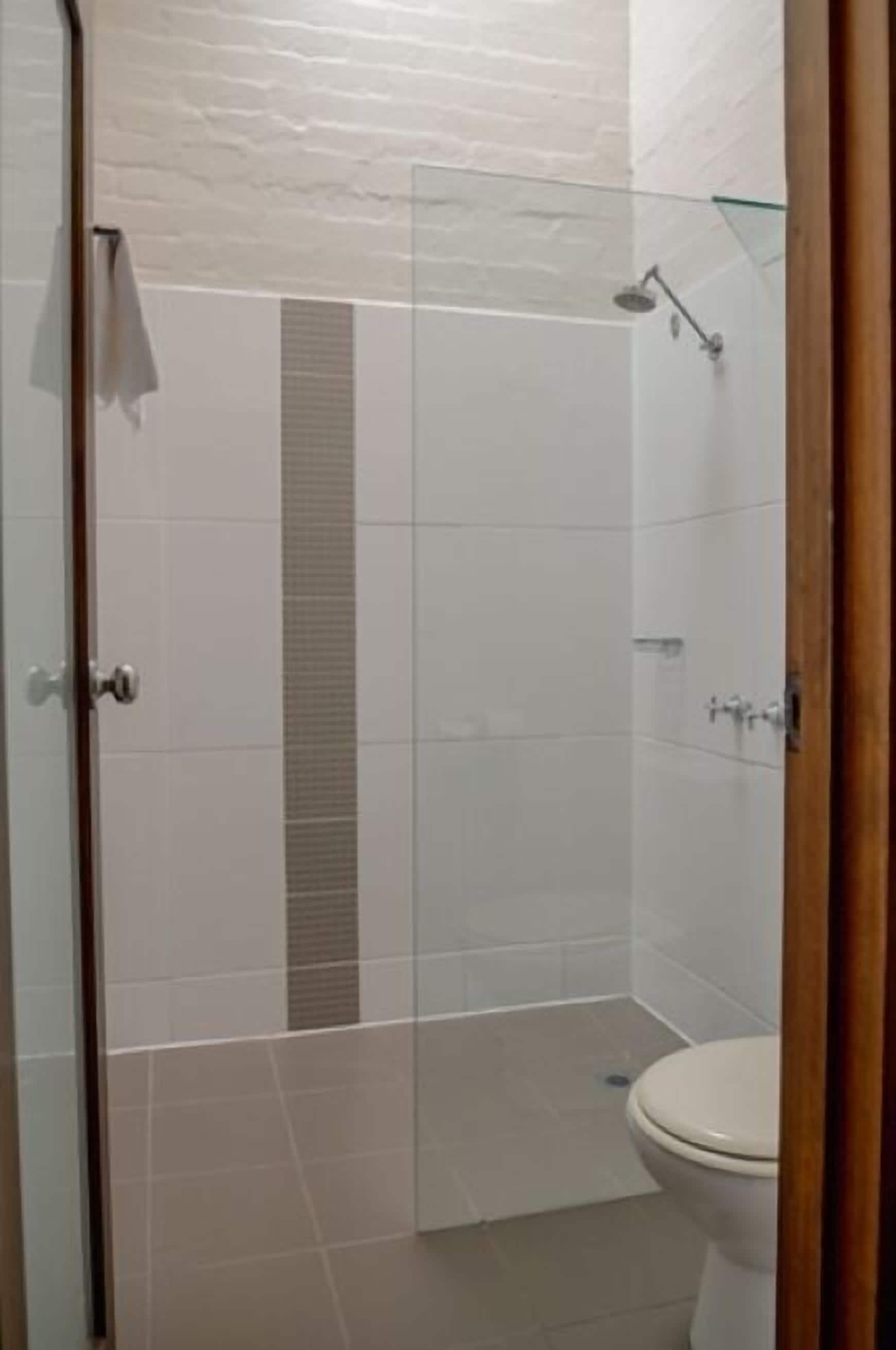 A bathroom with a glass shower enclosure, a toilet, and a white tiled floor.