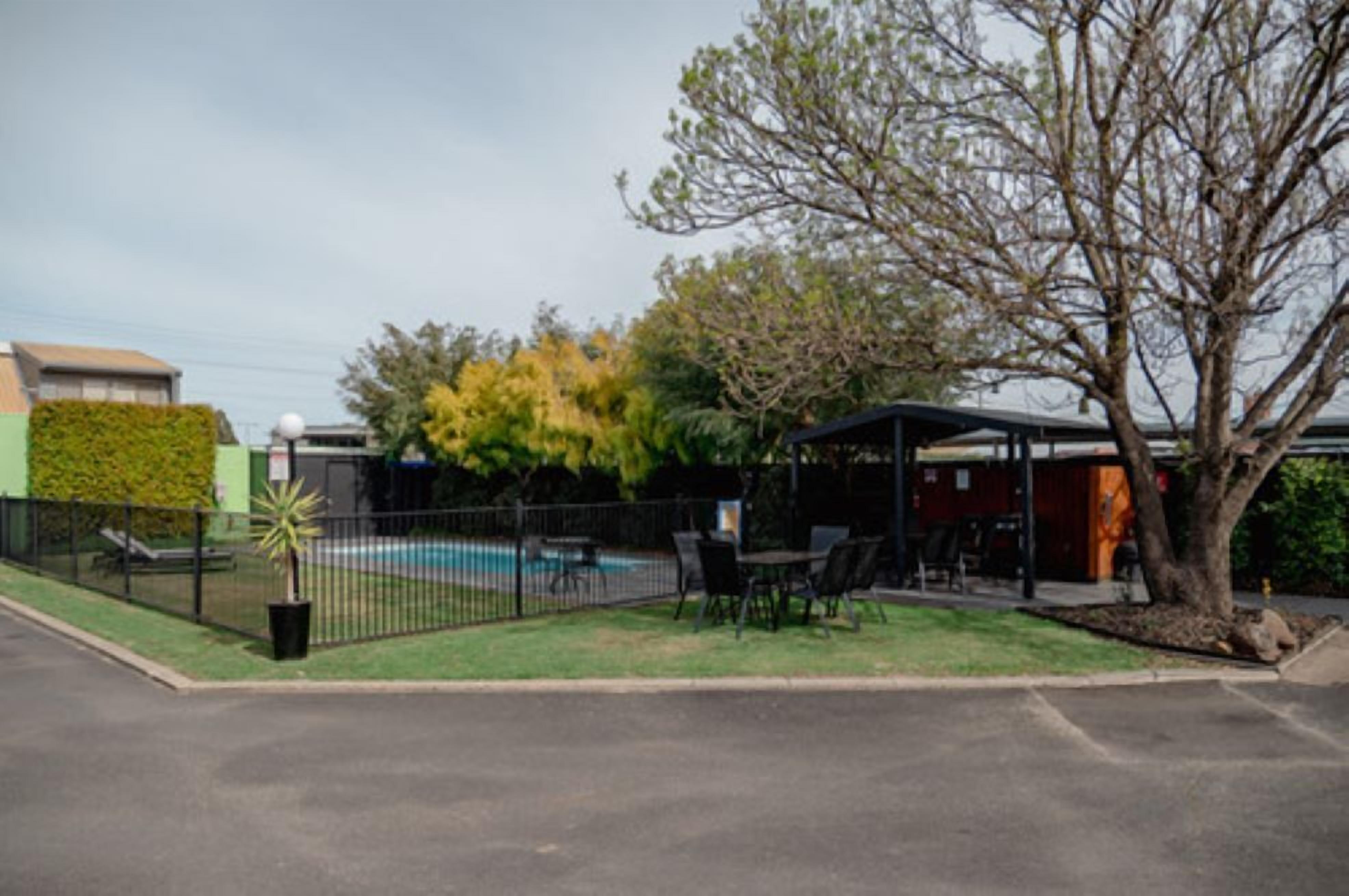A pool area with a fenced patio, outdoor seating, and a covered structure.