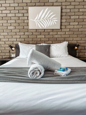 A neatly made bed with a grey blanket, pillows, and a folded towel. - Mitchell on Main Motel & Apartments (Bairnsdale)