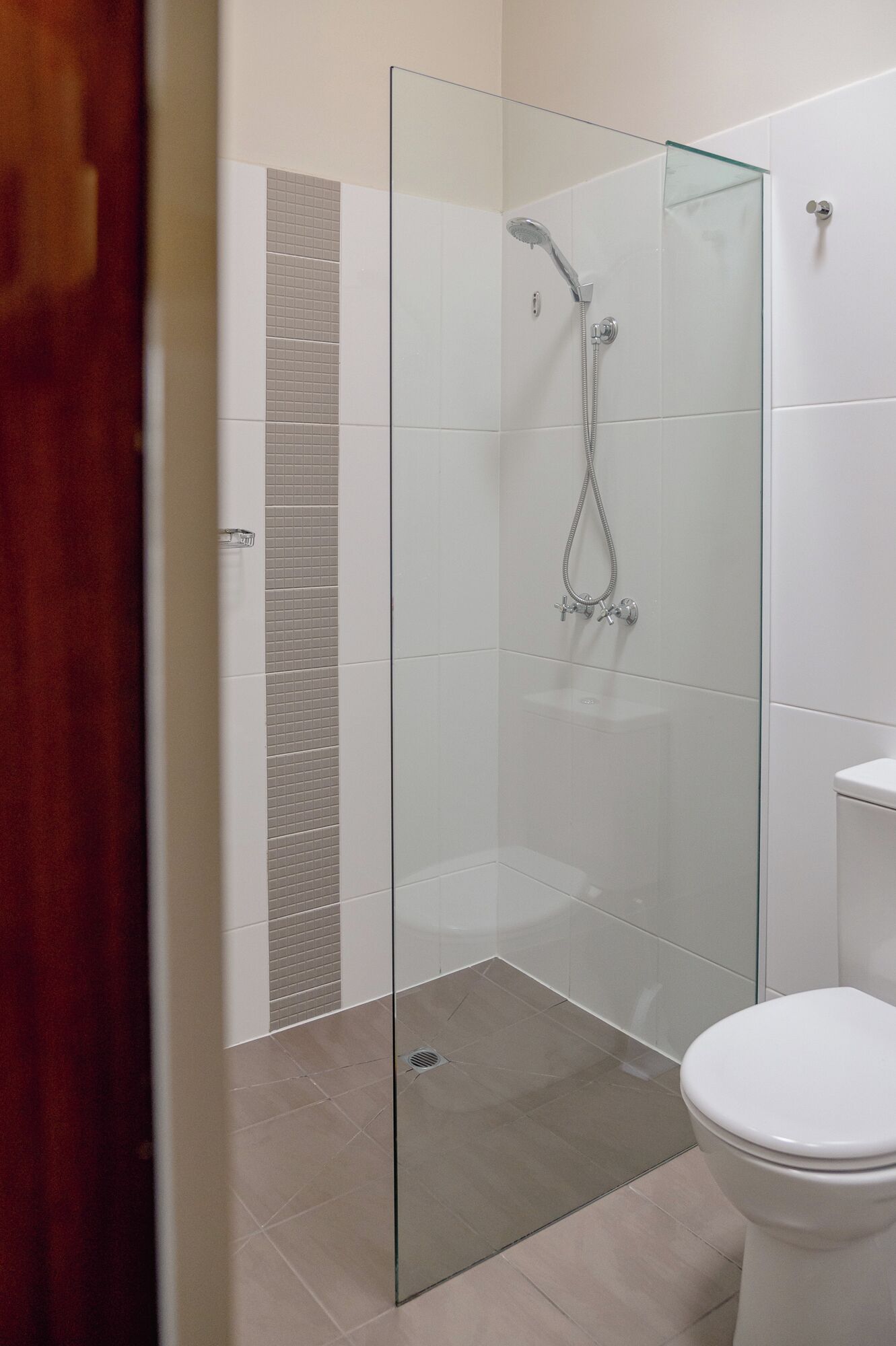 A modern bathroom with a glass-enclosed shower, a white toilet, and tiled walls.