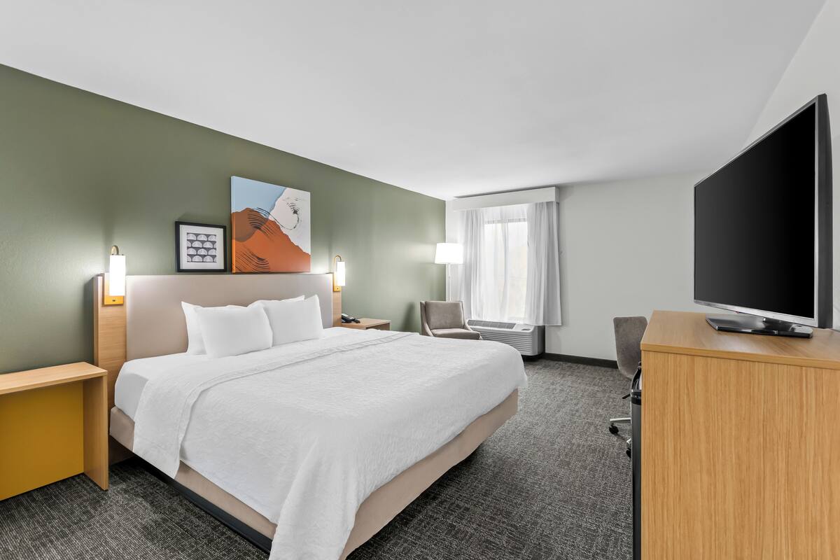 A hotel room with a large bed, a desk, a television, and a chair.