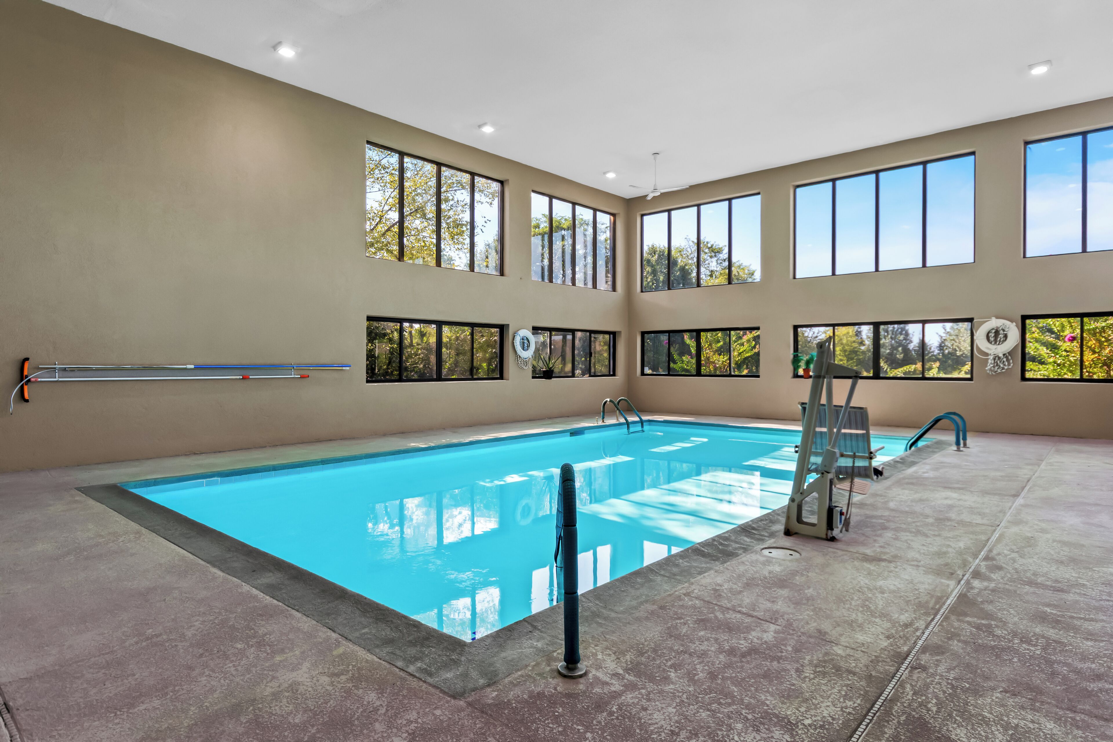 Une piscine à l’eau d’un bleu cristallin, entourée de grandes fenêtres qui offrent une vue sur les arbres et le ciel.