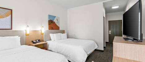 A hotel room with two beds, a desk, a television, and artwork on the walls.
