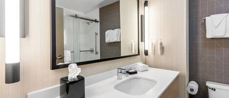 A modern bathroom with a large mirror, a sink, a toilet, and a shower.