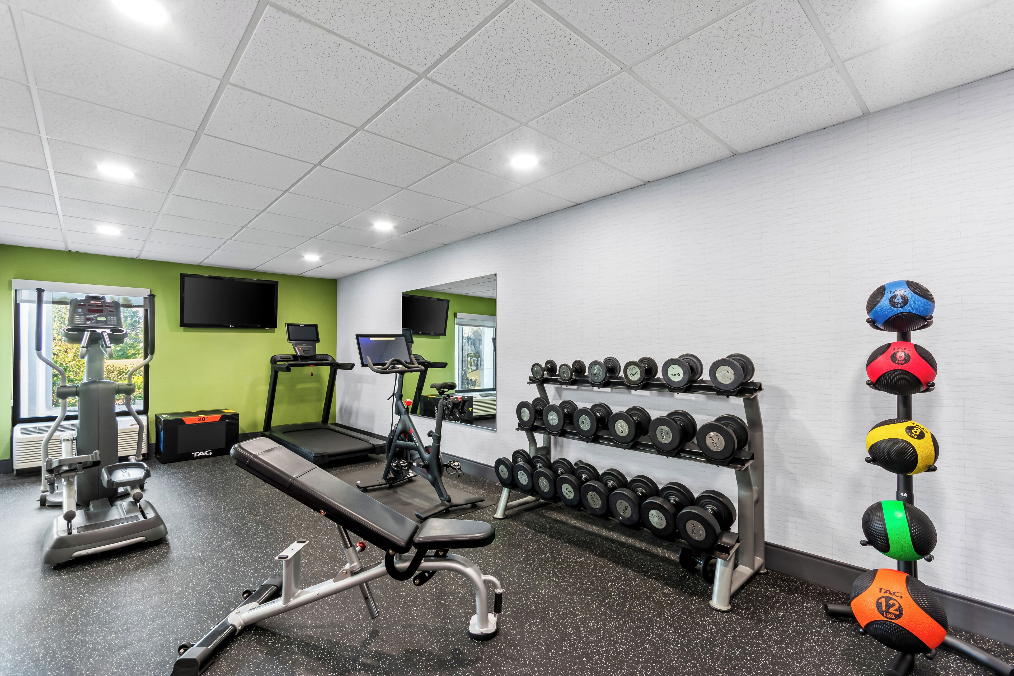 Une salle de sport équipée de matériel d’exercice, d’un tapis de course et d’un porte-haltères fixé au mur.