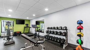 Une salle de sport équipée de matériel d’exercice, d’un tapis de course et d’un porte-haltères fixé au mur.