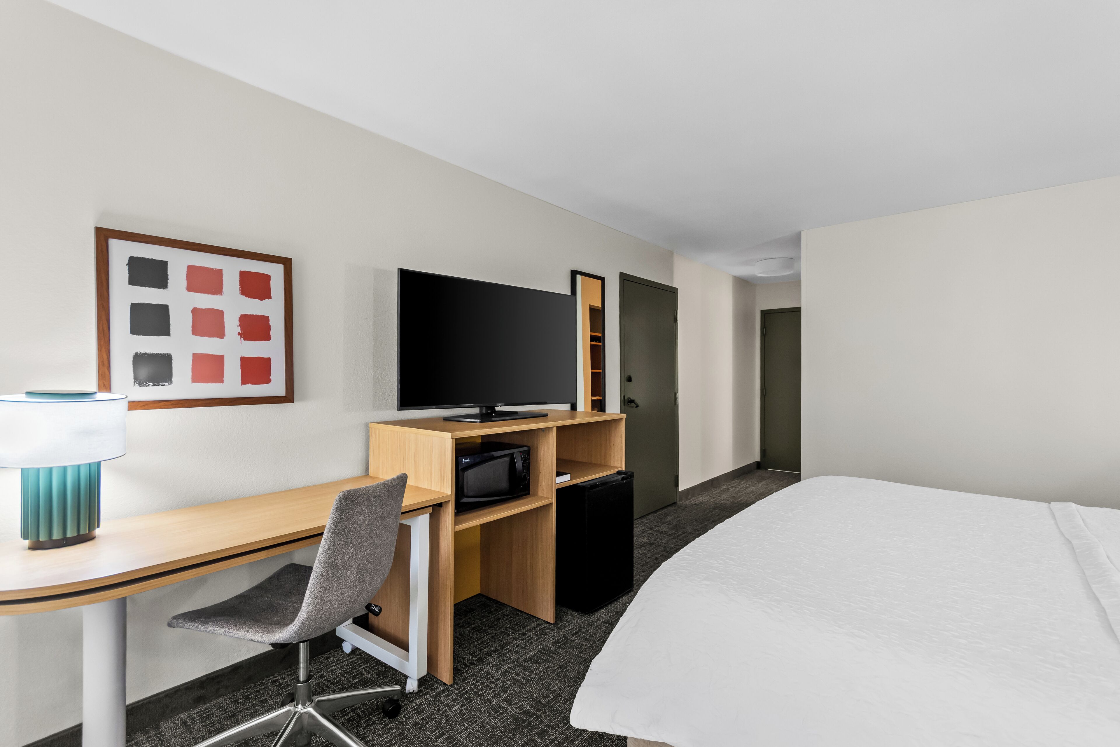 A hotel room with a bed, a desk with a chair, a television, a microwave, and a small refrigerator.