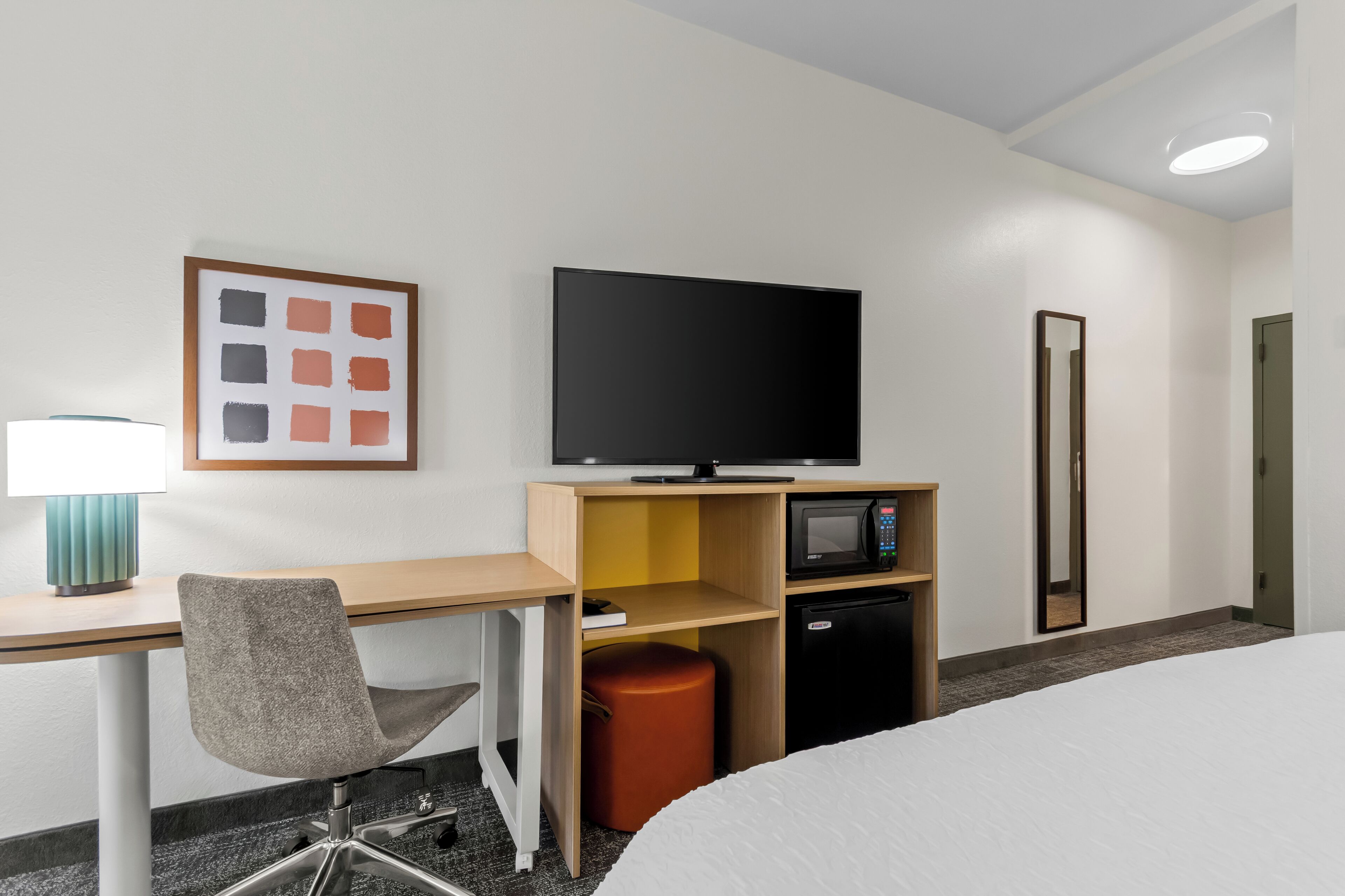 A hotel room with a bed, a desk with a chair, a television, a microwave, and a small refrigerator.