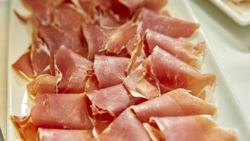 Un plato de carne curada en lonchas finas, probablemente jamón serrano, dispuesto ordenadamente sobre un plato blanco rectangular.
