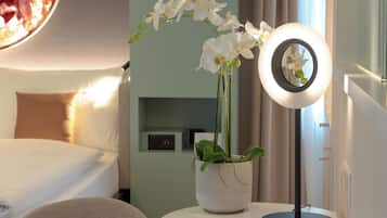 Una habitación de hotel con cama, una mesita de noche con lámpara y una orquídea en maceta.