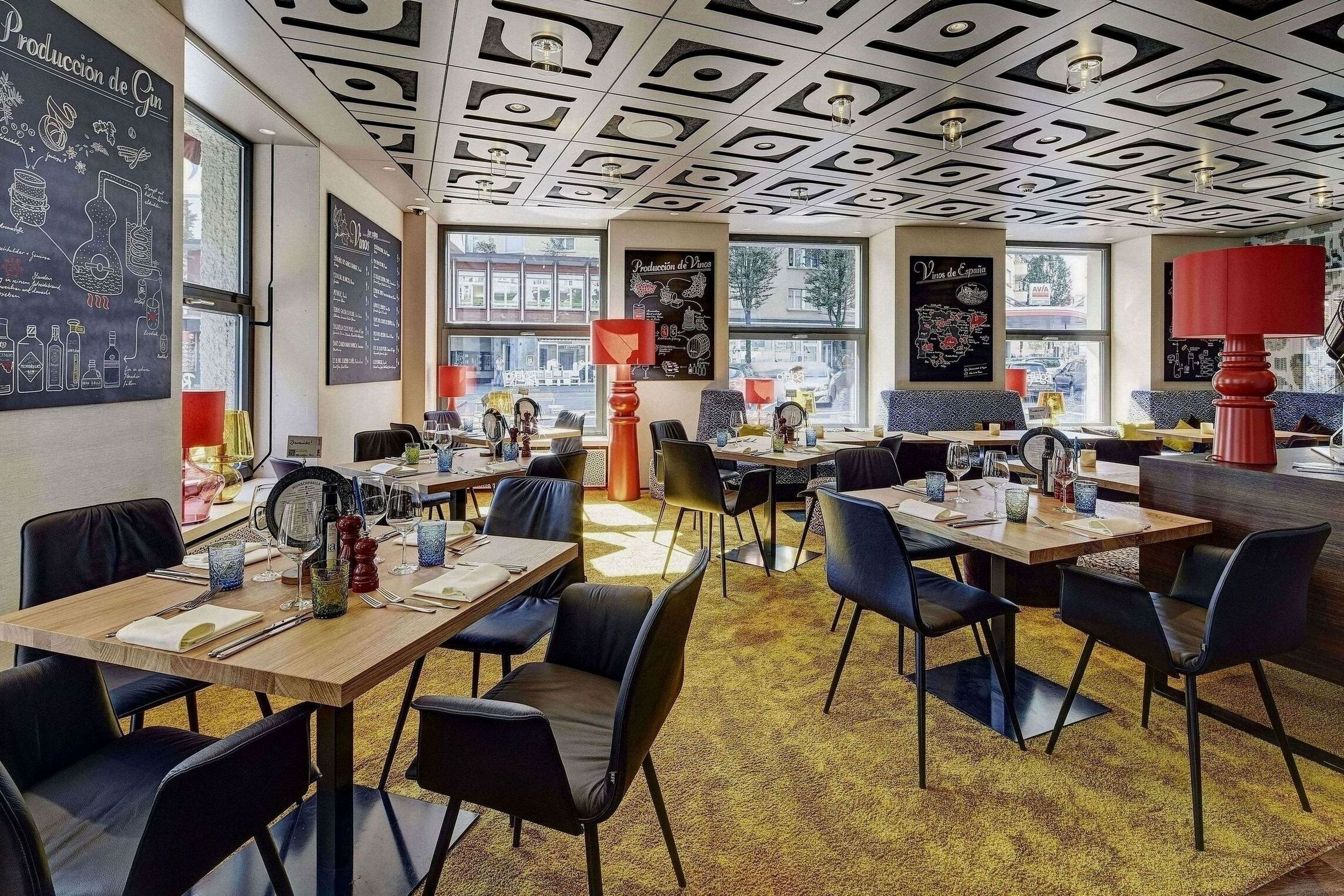 Un restaurante con varias mesas y sillas, techo decorado y amplios ventanales.