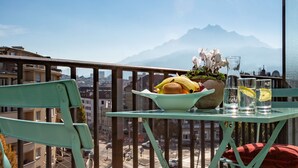 Un balcón con una mesa dispuesta para el desayuno, un cojín rojo y vistas a montañas.
