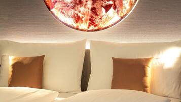 A hotel room with a large bed, two pillows, and a circular light fixture above the bed.