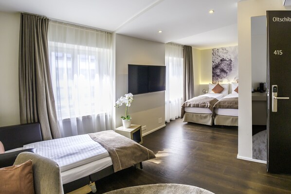 Habitación de hotel con dos camas, un televisor de pantalla plana, una mesita con una flor y una puerta con el número 415.