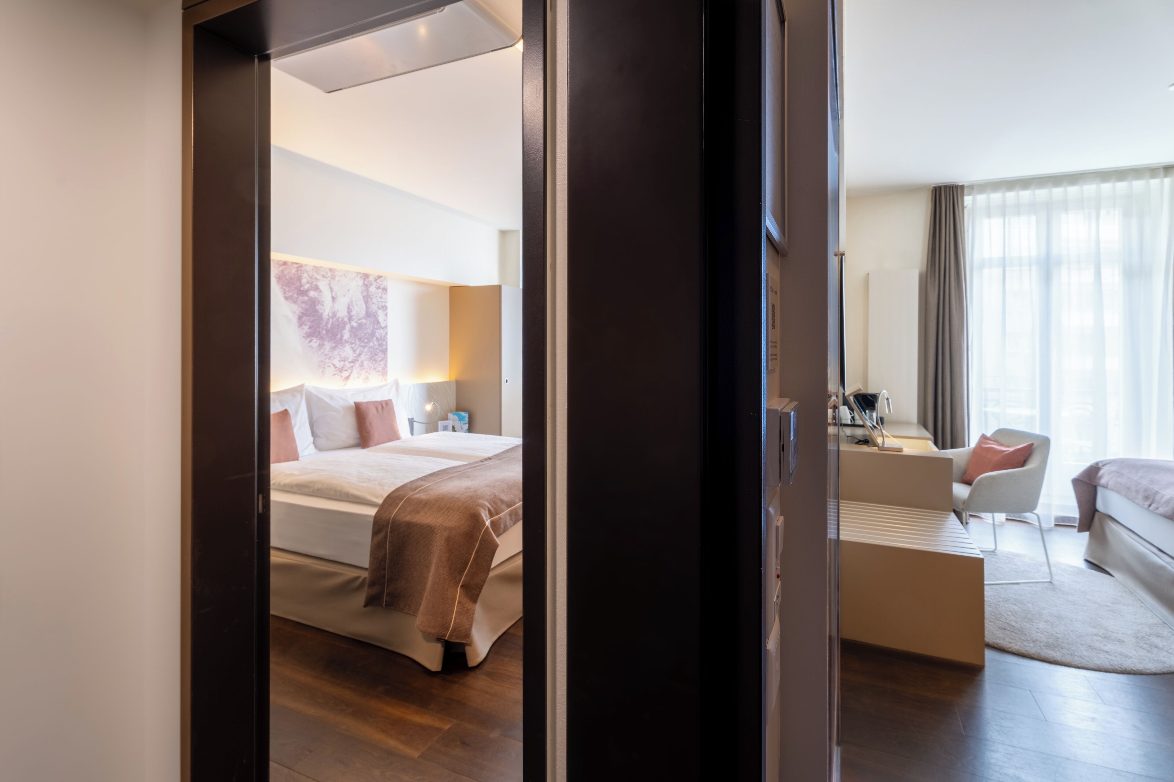Habitació d'hotel amb llit, taula de nit, làmpada i vista a la ciutat a través de la finestra.