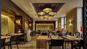 Un restaurante con mesas y sillas de madera, una lámpara central y un papel tapiz con diseño.