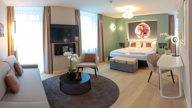 Una habitación de hotel moderna con sofá, una mesa redonda, cama, escritorio y un ventanal grande.