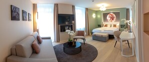 Una habitación de hotel moderna con sofá, una mesa redonda, cama, escritorio y un ventanal grande.
