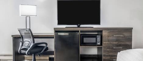 Habitació d'hotel moderna amb escriptori, cadira, televisió, microones i un llit.