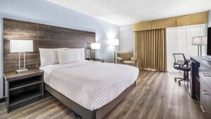 Une chambre d’hôtel avec un grand lit, des lampes de chevet, une chaise, un bureau avec une chaise et une grande fenêtre avec des rideaux.