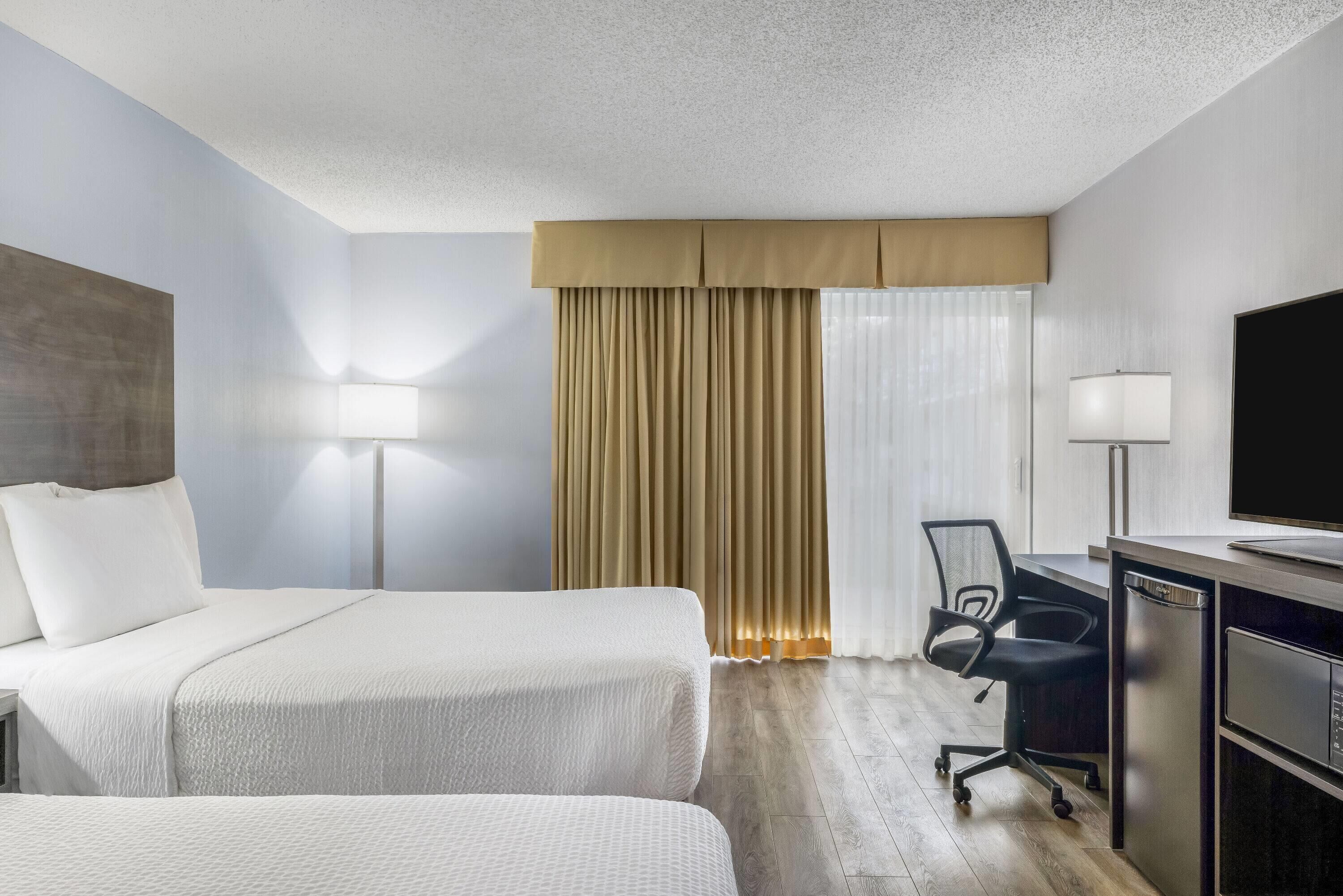 Une chambre d’hôtel avec deux lits, un bureau avec une chaise, une télévision et une fenêtre avec des rideaux.
