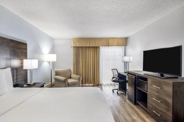 A hotel room with a bed, desk, chair, television, and a minibar.