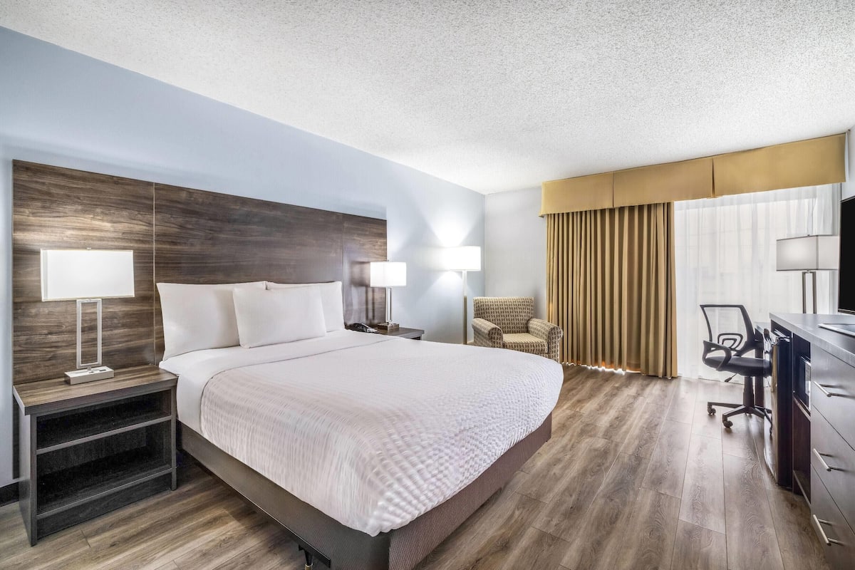 A hotel room with a large bed, bedside tables, a desk with a chair, and a TV.