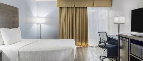 Habitación de hotel con dos camas, un escritorio con silla, televisor y ventana con cortinas.