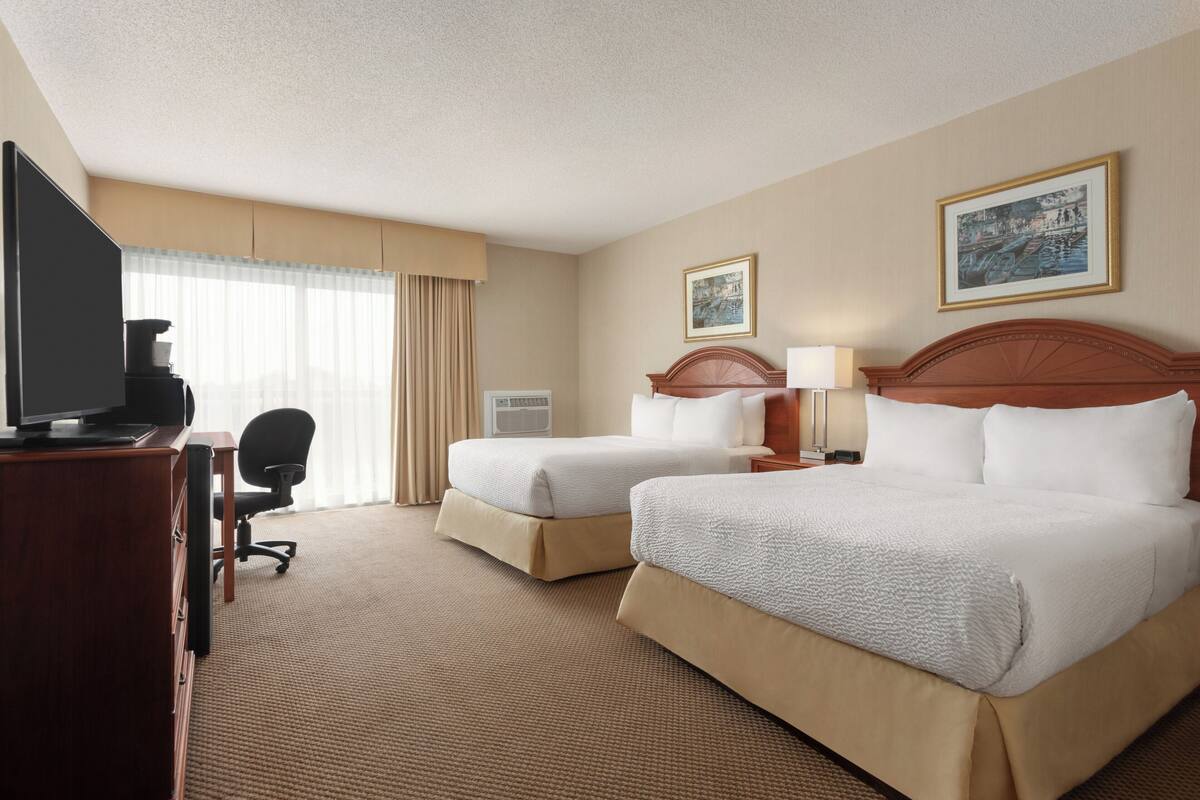 A hotel room with two beds, a desk with a television, a chair, and a window with curtains.