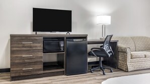 Une chambre d’hôtel équipée d’un bureau, d’une télévision, d’un four à micro-ondes, d’un réfrigérateur, d’une chaise et d’un canapé.