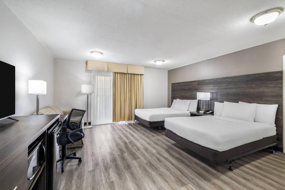 A hotel room with a bed, two bedside tables, a desk with a chair, a TV, and a window with curtains.