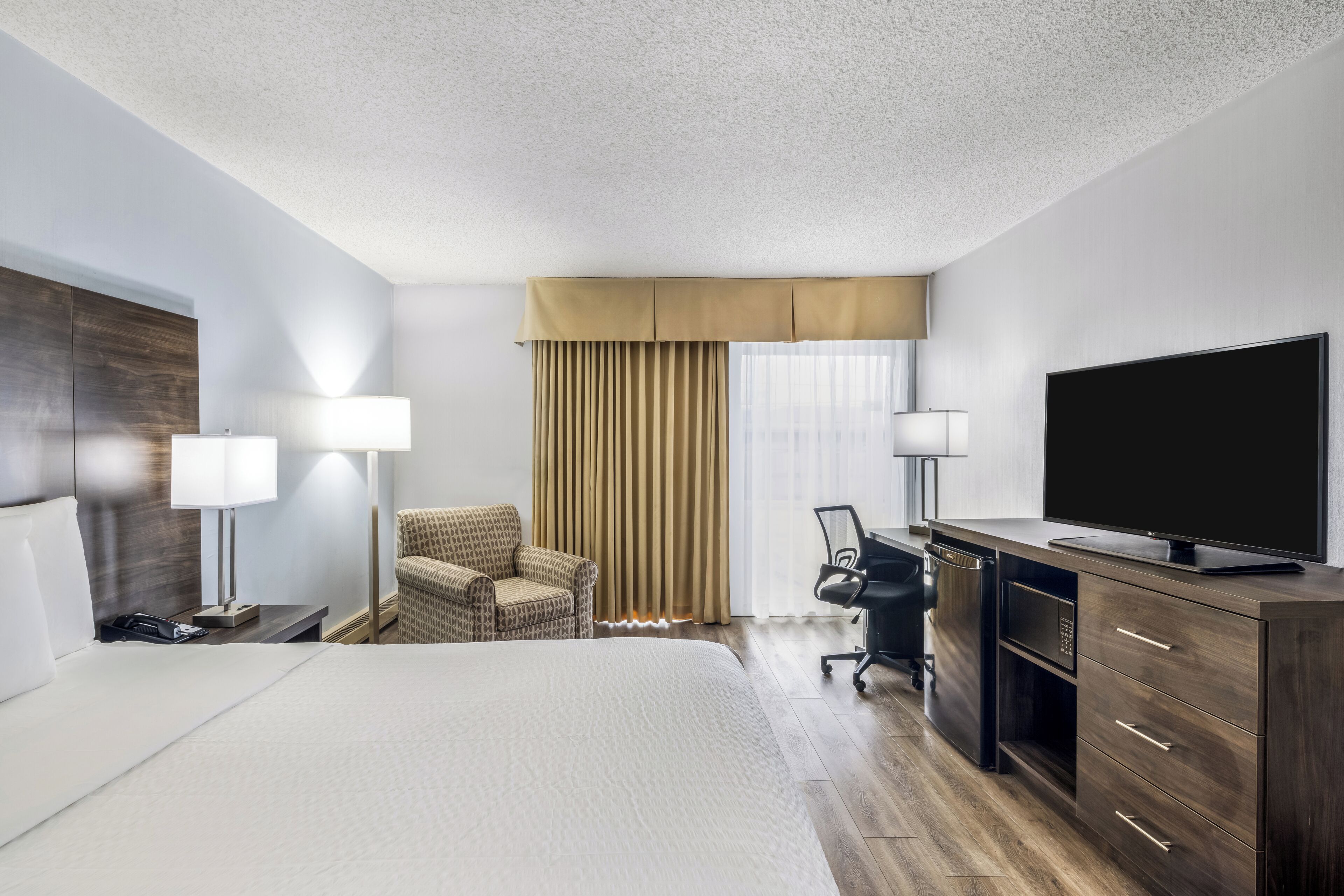 A hotel room with a bed, a desk, a chair, a television, and a window with curtains.