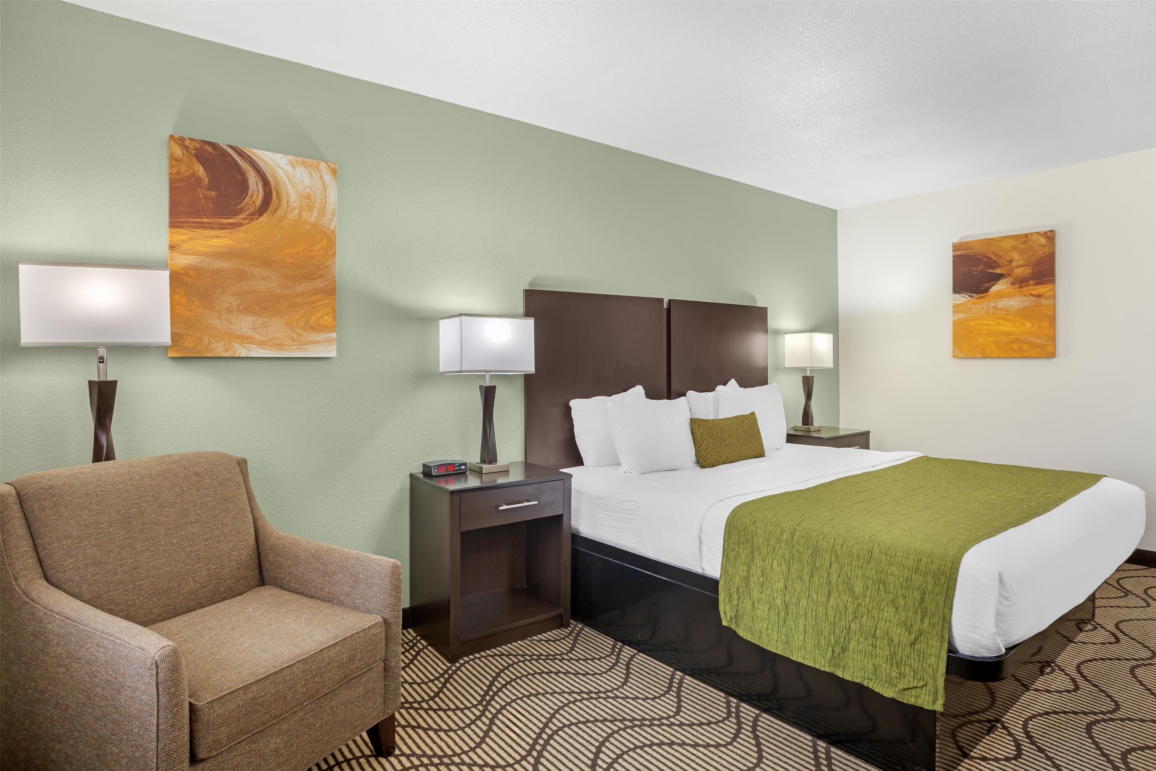 A hotel room with a bed, a chair, a nightstand, and two wall-mounted lamps.