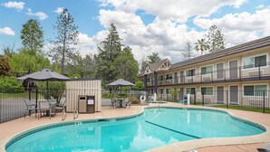 A swimming pool with lounge chairs and umbrellas, surrounded by a fence and trees. - Best Western Gold Country Inn (Grass Valley)