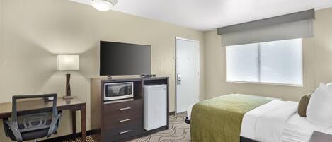 Habitación de hotel con cama, escritorio con silla, televisión, microondas y refrigerador.