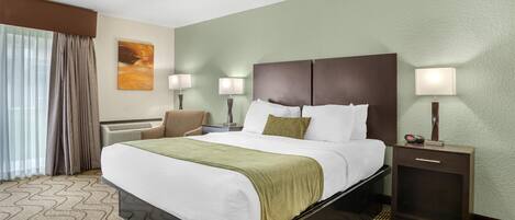 A hotel room with a large bed, two bedside tables with lamps, a chair, a painting on the wall, and a patterned carpet.