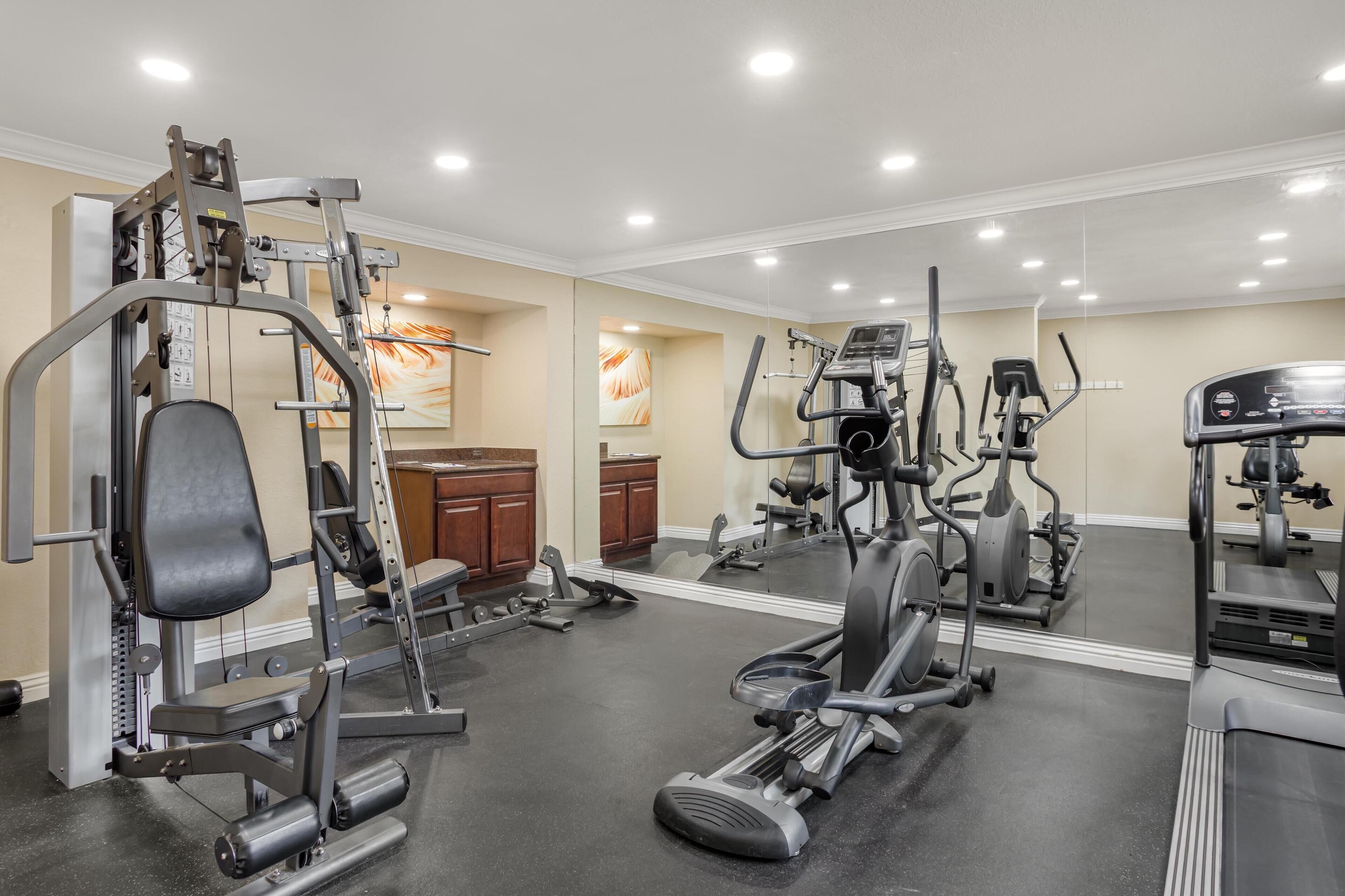 Een sportschool met diverse fitnessapparaten, waaronder een halterbank, een crosstrainer en een hometrainer.