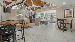 A spacious indoor area with a high ceiling, wooden beams, a kitchen area, and a dining area with chairs and tables. - Best Western Gold Country Inn (Grass Valley)