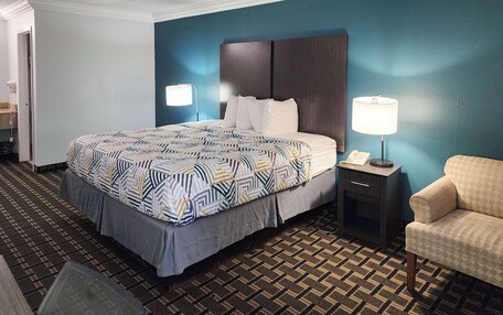 A hotel room with a large bed, two bedside lamps, a chair, and a small table with a phone.