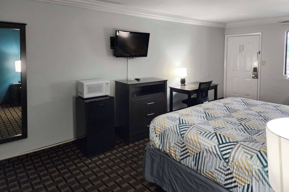 A hotel room with a bed, a desk, a television, a microwave, and a door.