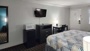 A hotel room with a bed, a desk, a television, a microwave, and a door.