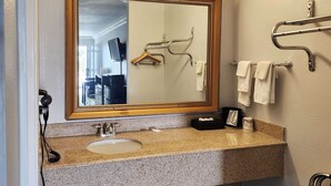 Une salle de bain dotée d’un lavabo avec un plan de travail en granit, d’un grand miroir, d’un porte-serviettes et d’une douchette à main.
