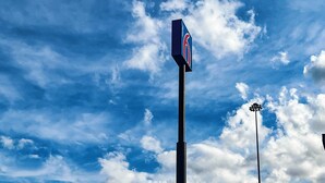 Un ciel bleu dégagé, parsemé de nuages, et un panneau fixé sur un poteau.