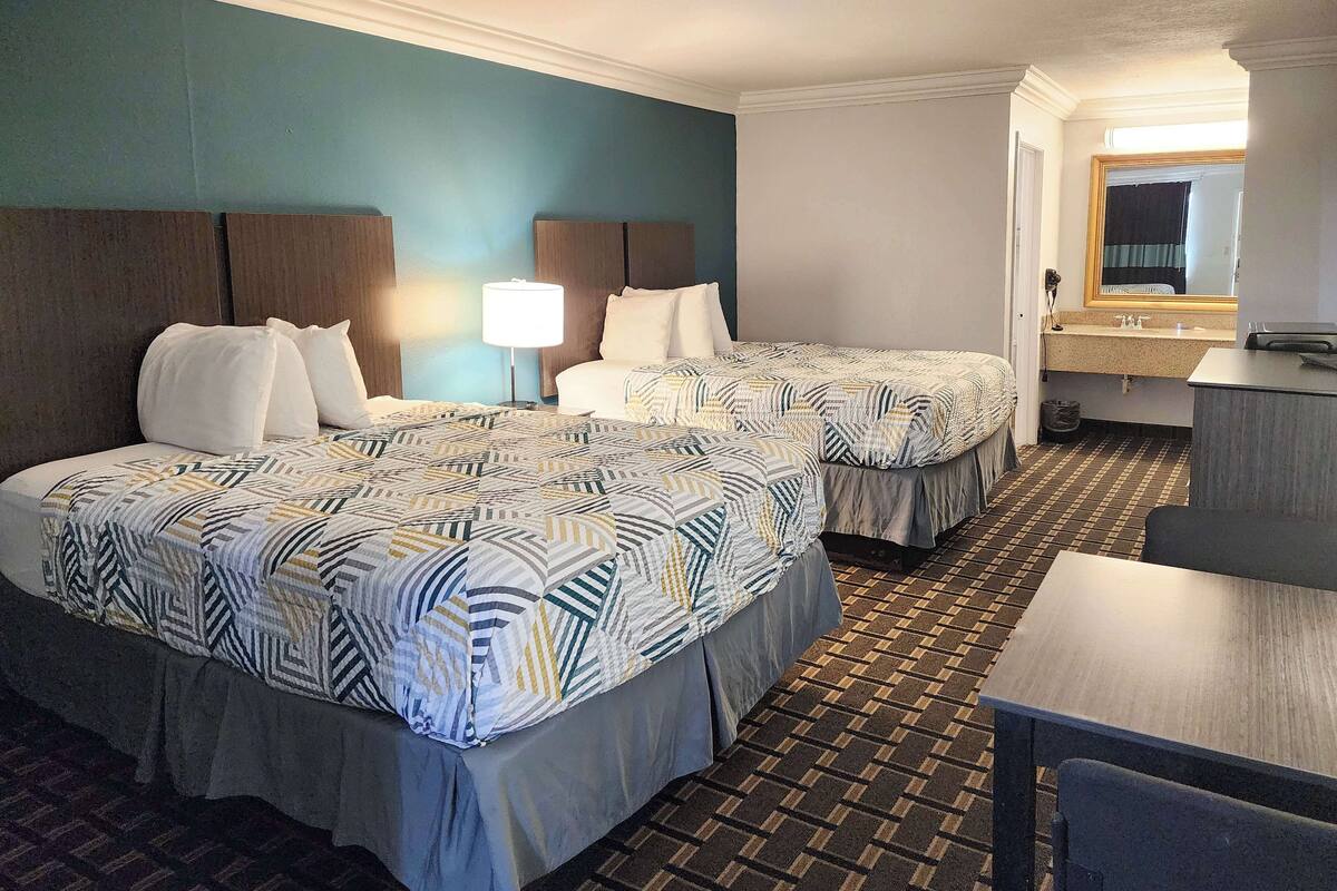 A hotel room with two beds, a desk, a mirror, and a bathroom visible through an open door.