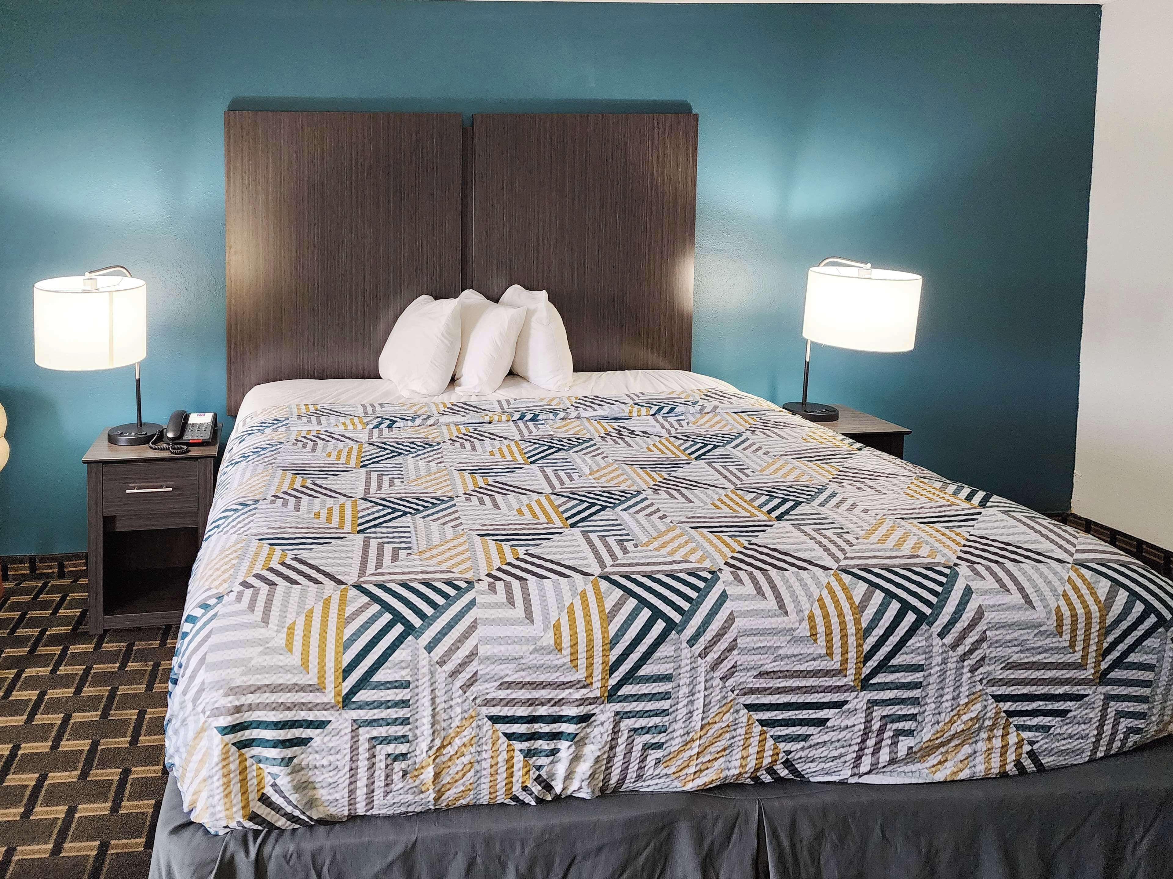 A neatly made bed with a patterned bedspread, two bedside lamps, a nightstand with a phone, and a dark wooden headboard.