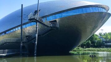 A modern building with a unique curved design, a staircase leading to an upper level, and a body of water in front.