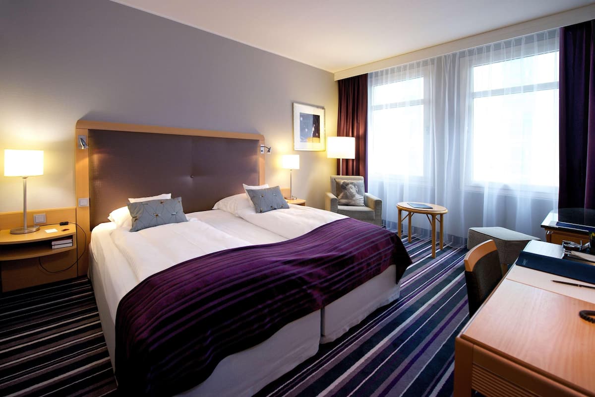 A hotel room with a large bed, bedside tables, a desk, and a chair.