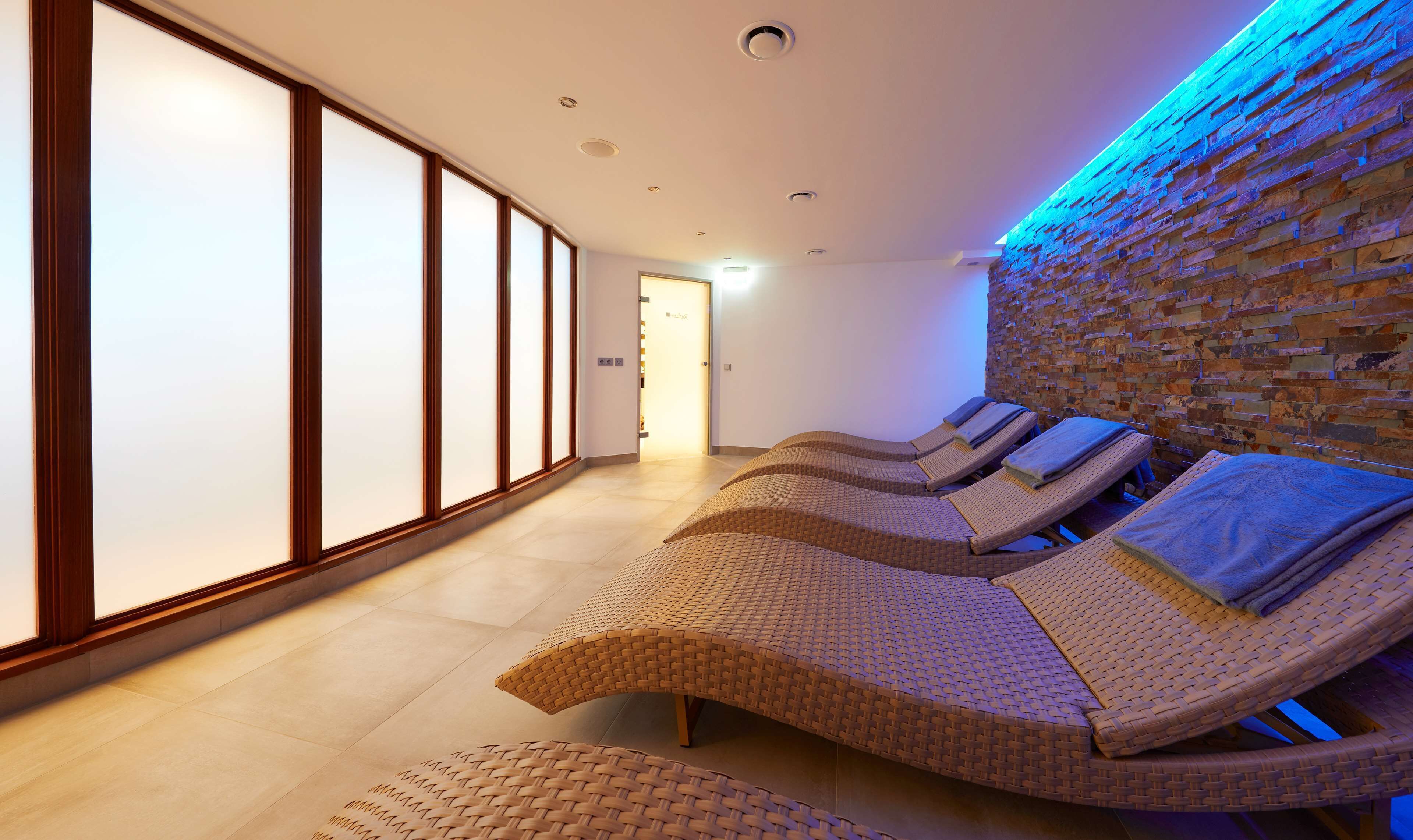 A spa room with four reclining chairs, a stone wall, and a sliding door.