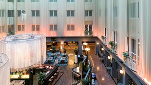 Un amplio vestíbulo de hotel con varias zonas de comedor, una escalera central y vistas al cielo a través del techo.